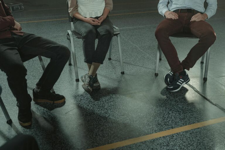A group of three adults sitting in chairs during a discussion or support session indoors.