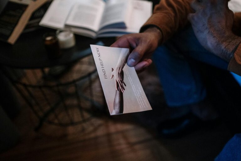 A person holds a help brochure in a cozy indoor setting, symbolizing support and mental health awareness.