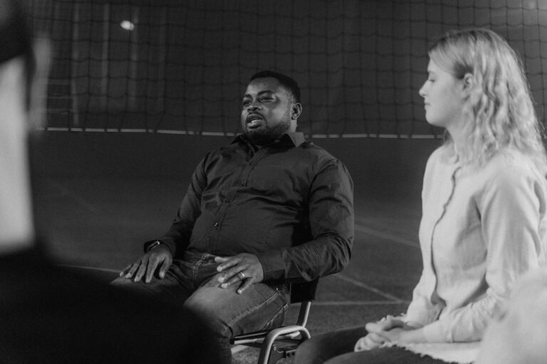 Black and white image of individuals engaged in a support group discussion indoors.